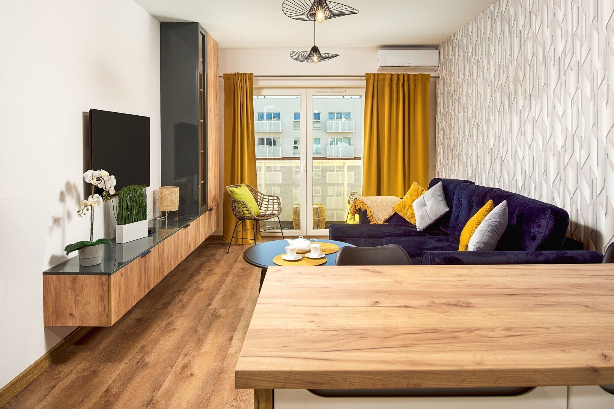 Un espacio de estar moderno con un sofá, una mesa de comedor y vistas al exterior a través de grandes ventanales.