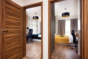 Ein Hotelzimmer mit Holzboden, einem Bett mit gelber Bettdecke, einem Schreibtisch mit Stuhl und einer Pendelleuchte.