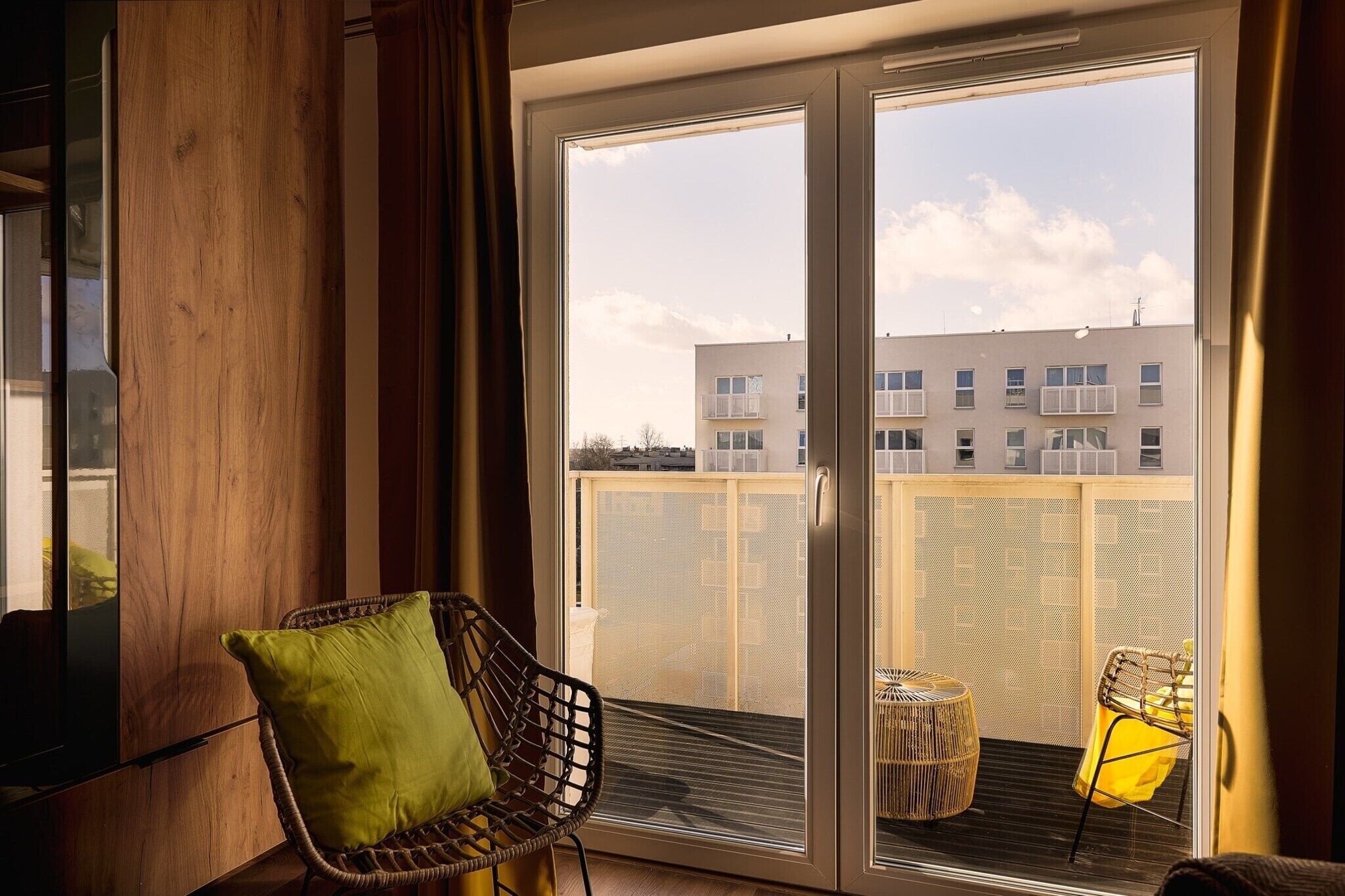 Ein Balkon mit einem Korbstuhl, einem kleinen Tisch, einem Metallgeländer und einem Gebäude im Hintergrund.