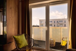 A balcony with a wicker chair and a small table, a metal fence, and a building in the background. - City View Apartment in Łódź for 6 Guests (Łódź)