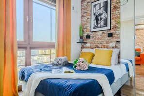 Ein Schlafzimmer mit einem großen Bett, einer Backsteinwand, einem Fenster und Blick auf Gebäude.