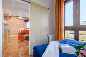 Un dormitorio moderno con un ventanal grande, una cama con cubrecama azul y vistas a la ciudad.