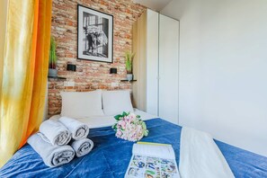 Une chambre d’hôtel avec un mur en briques, un lit avec des serviettes pliées, un bouquet de fleurs et un magazine.