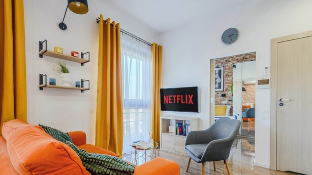 A modern living room with a sofa, a television displaying 'NETFLIX,' and a bookshelf. - Siedmiogrodzka Flat with Views (Warszawa)