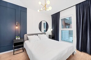 A modern bedroom with a large bed, a bedside table, a mirror, a window with curtains, and a unique ceiling light fixture. - Elegant Apartment near Central Museum of Textiles (Łódź)