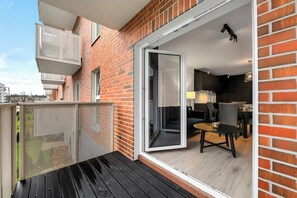 A modern apartment with a sliding glass door leading to a balcony, a small dining area with a table and chairs, and a kitchen visible through the open door. - Elegant Apartment near Vitsula River (Łódź)