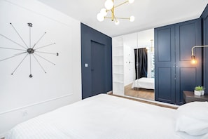 A modern bedroom with a large bed, a wall clock, and a mirror. - Elegant Apartment near Vitsula River (Łódź)