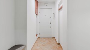 Un couloir étroit, avec une porte blanche au fond, un banc sur la gauche et un climatiseur fixé au mur au-dessus de la porte.