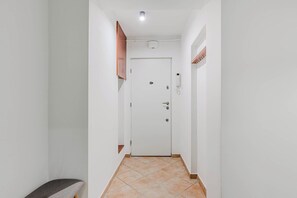 A narrow hallway with a white door at the end, a bench on the left, and a wall-mounted air conditioning unit above the door. - House in Brélès near Rock Beach & Amusement Park (Warszawa 2)