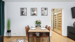 Un coin repas avec une table dressée pour quatre personnes, entourée de chaises, et agrémenté d’un vase de fleurs et de verres à vin posés sur la table.