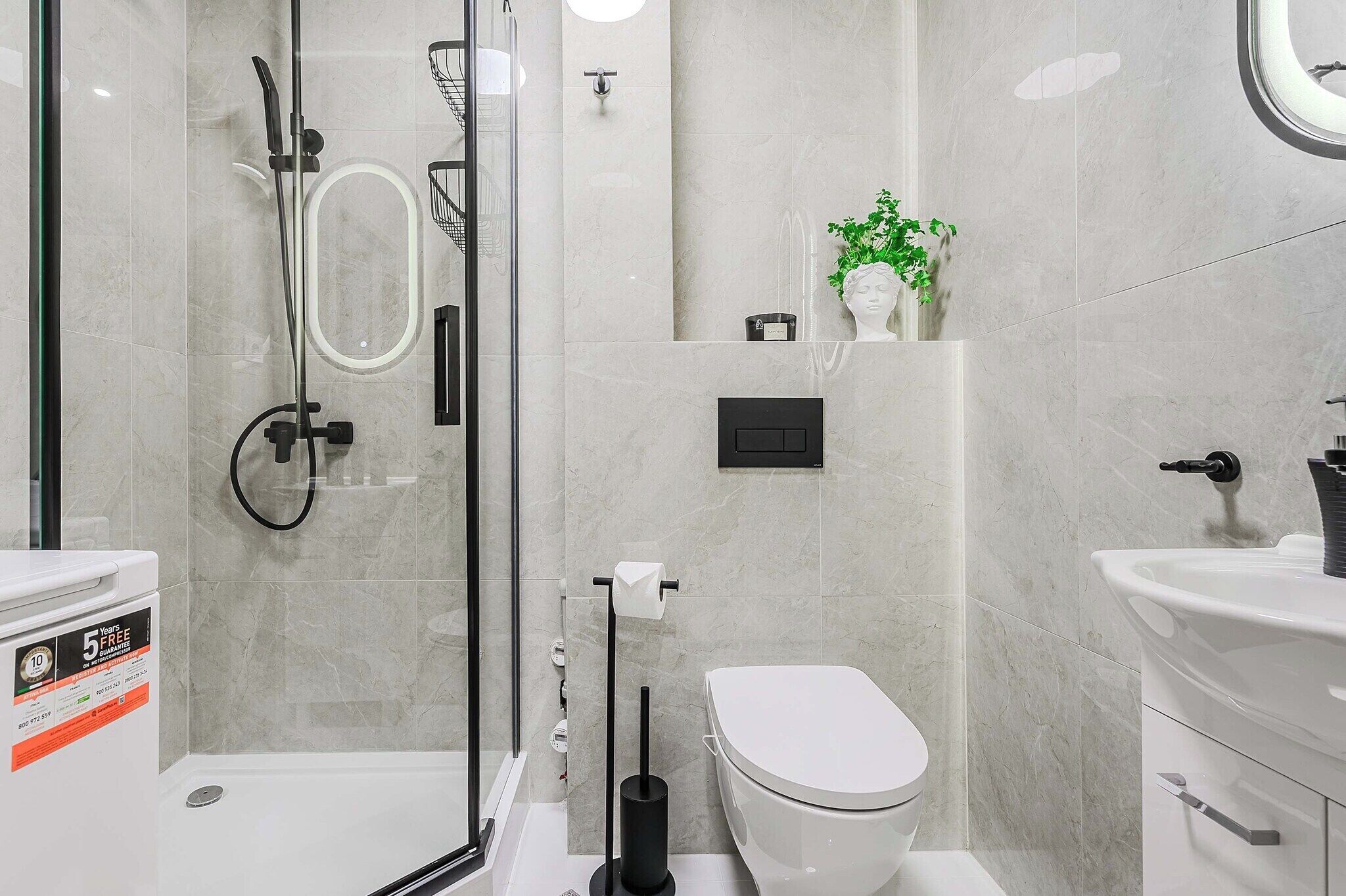Et moderne badeværelse med en glasafskærmet brusekabine, toilet, håndvask og en lille plante på væggen.