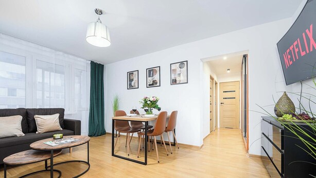 Un salon moderne comprenant un canapé, une table basse, une table à manger et des chaises. Un téléviseur est fixé au mur et une porte donne accès à une autre pièce.