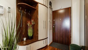 A hallway with wooden cabinets, a potted plant, a door with a handle, and a green bench. - Flat near Metro, Warsaw (Warszawa)