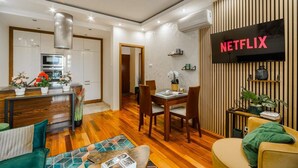 A modern living room with a dining area, a kitchen, and a wall-mounted TV displaying 'NETFLIX'. - Flat near Metro, Warsaw (Warszawa)
