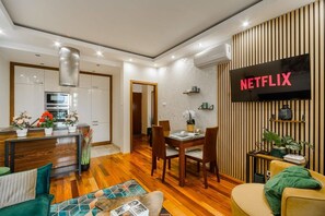 Ein modernes Wohnzimmer mit Essbereich, einer Küche und einem an der Wand befestigten Fernseher, der 'NETFLIX' anzeigt.