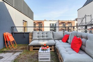 Ein Außenbereich mit einer grauen Couch, roten Kissen und einem kleinen Tisch mit Gläsern und Wassermelone.
