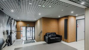 Ein Empfangsbereich mit einer schwarzen Ledersitzgruppe, Fliesenboden, Backsteinwand und einer Decke mit Gitterstruktur.