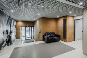 Ein Empfangsbereich mit einer schwarzen Ledersitzgruppe, Fliesenboden, Backsteinwand und einer Decke mit Gitterstruktur.