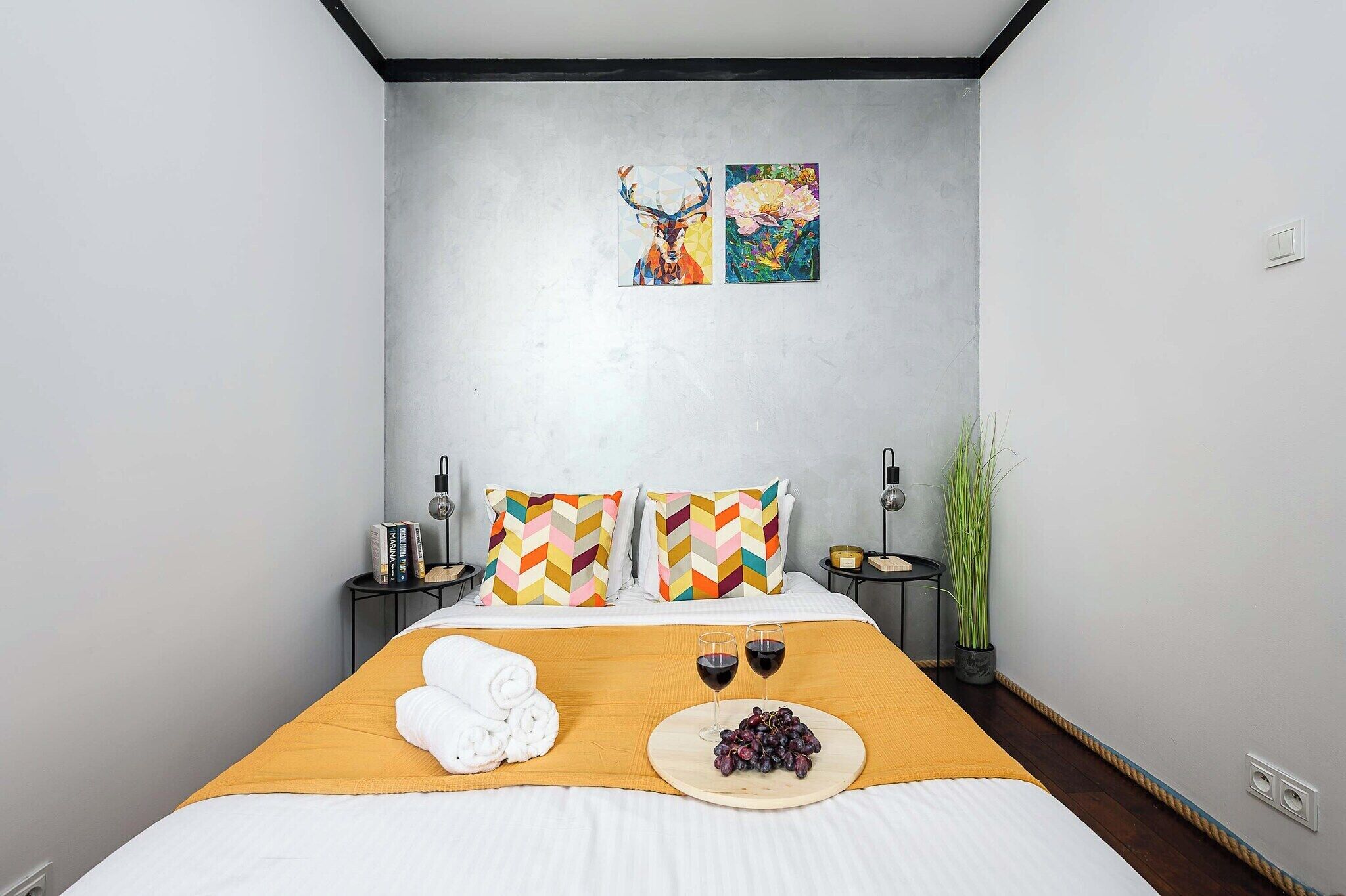 A modern hotel room with a bed, a side table with a lamp, and a wall-mounted artwork.