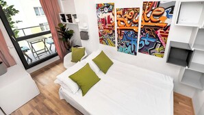 Une chambre moderne avec un lit, des oreillers, une petite table, une plante en pot et un balcon avec vue.