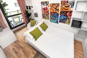Ein modernes Schlafzimmer mit Bett, Kissen, einem kleinen Tisch, einer Topfpflanze und einem Balkon mit Aussicht.