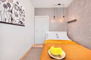 A bedroom with a bed, a bedside table with a yellow cloth, a wall-mounted light fixture, and a door. - Home near Warsaw Spire (Warszawa 2)