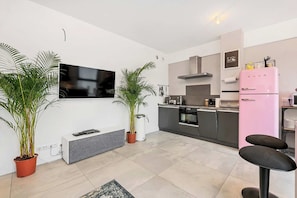 Eine moderne Küche mit Fernseher, einem pinken Kühlschrank und einer Essecke mit zwei Hockern.