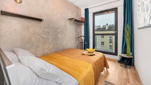 Une chambre à coucher avec un lit, une fenêtre avec des rideaux, un luminaire suspendu et une étagère fixée au mur.