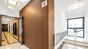Un couloir d’hôtel moderne avec un mur en bois, une enseigne indiquant le numéro de la chambre 6 et une vue sur l’extérieur à travers une grande fenêtre.