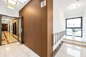 A modern hotel corridor with a wooden wall, a sign indicating room number 6, and a view of the outside through a large window.