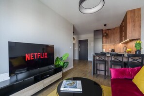Ein modernes Wohnzimmer mit Flachbildfernseher, der 'NETFLIX' anzeigt, und einem Essbereich mit Holzmöbeln.