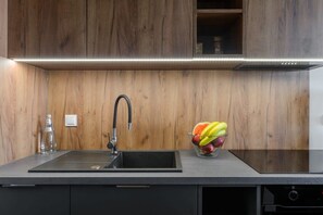 Une cuisine moderne avec un évier noir, un robinet en acier inoxydable et un saladier rempli de fruits posé sur le plan de travail.