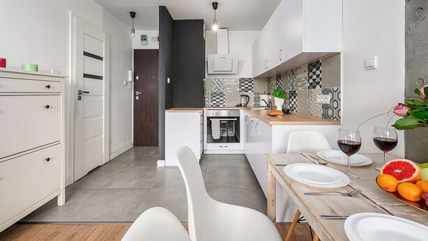 A modern kitchen with white cabinetry, a dining area with a wooden table, and a built-in oven. - Sunlit Home with City Views (Warszawa)