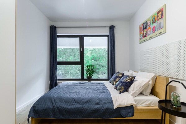 Ein Schlafzimmer mit einem Bett, einem Fenster, einer Pflanze und einem Wandbild.