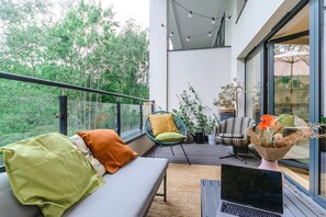 Ein Balkon mit einer Couch, Stühlen, einem Laptop und Blumentöpfen.