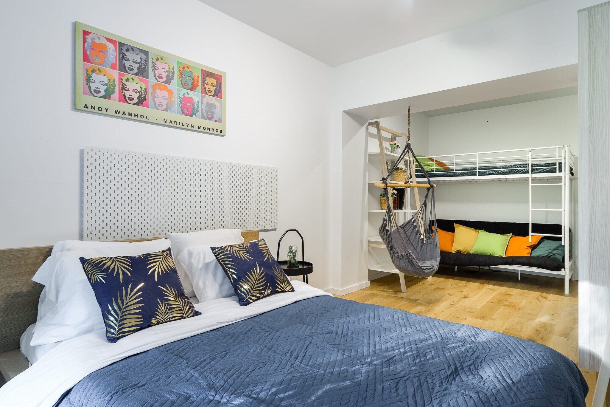 A bedroom with a bunk bed, a hanging chair, a bed with patterned pillows, a headboard with a perforated design, and a wall art piece.