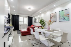 A modern living room with a red sofa, a dining area with white chairs, and a kitchen with a stainless steel sink. - Spacious Central Warsaw Apartment (Warszawa 2)