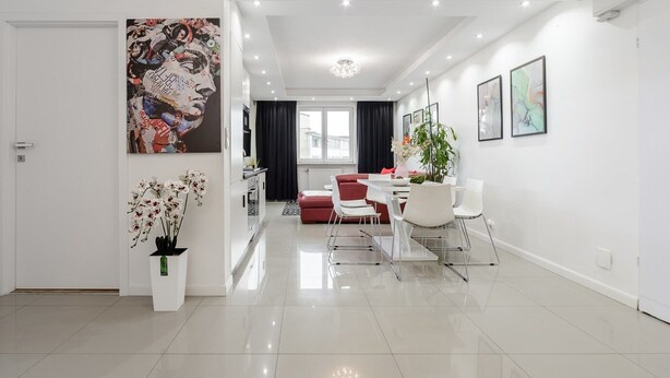 Una sala de estar moderna con comedor, un sofá rojo, sillas blancas y un cuadro abstracto grande.