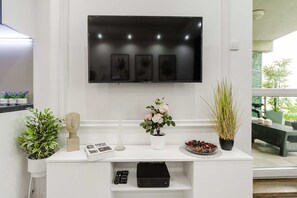 Ein modernes Wohnzimmer mit einem an der Wand befestigten Flachbildfernseher, einem weißen Konsolentisch mit Dekoration und Blick ins Freie durch ein großes Fenster.