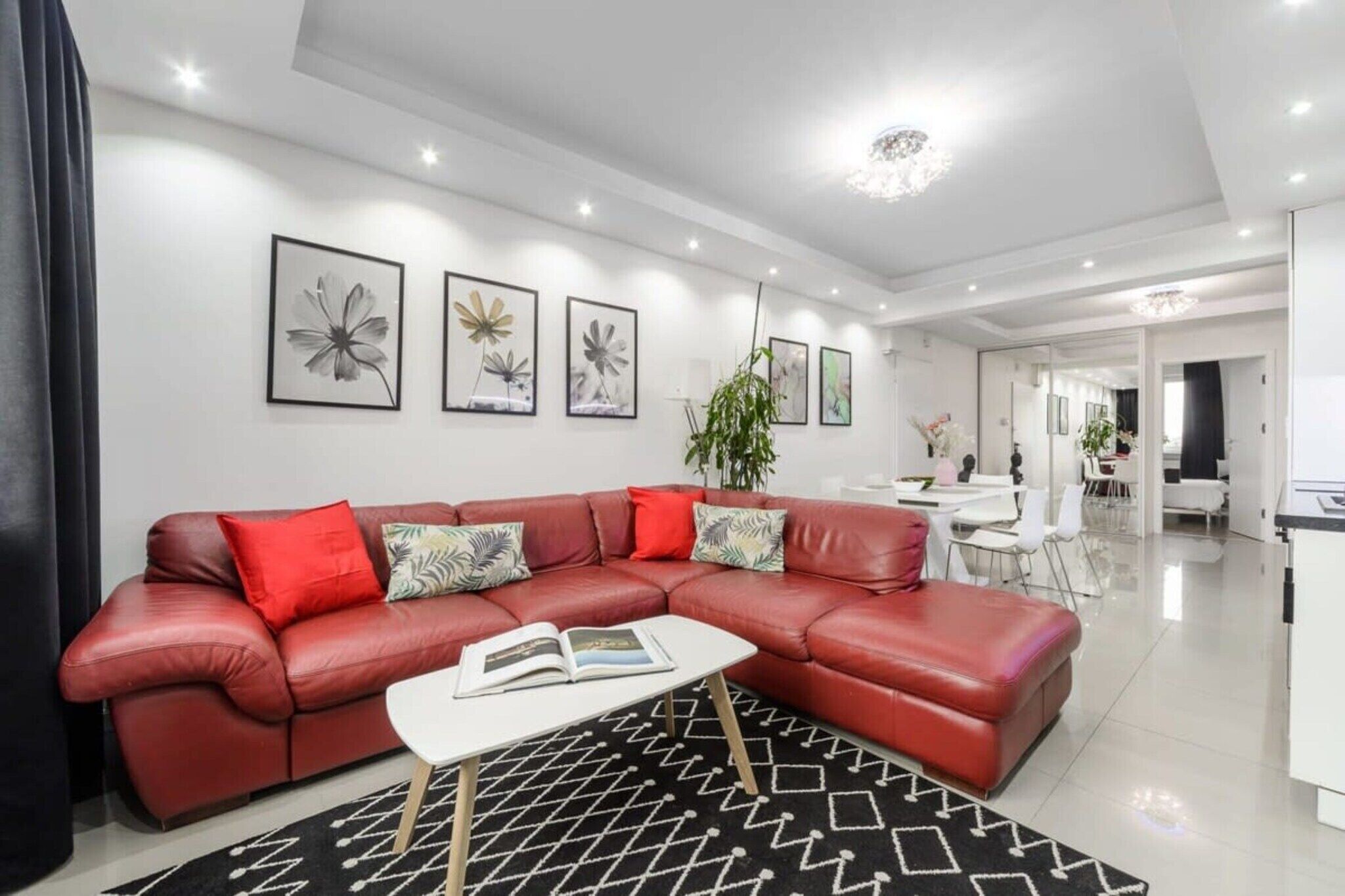 A modern living room with a red leather sofa, a white coffee table, and a black and white patterned rug.