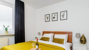 Una habitación de hotel con cama, mesita de noche, lámpara, florero y ventana con cortinas.