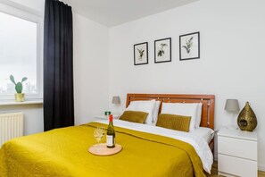 Ein Hotelzimmer mit Bett, Nachttisch, Lampe, Blumenvase und einem Fenster mit Vorhängen.