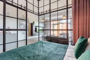 Ein Zimmer mit Bett, Blick durch ein Fenster mit Vorhang und einer Wand mit Riffelung.