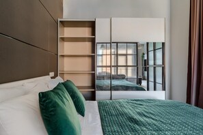 A modern bedroom with a bed, green pillows, a headboard, a built-in wardrobe, and a large window with a view. - Loft Flat in Historical Area (Łódź)
