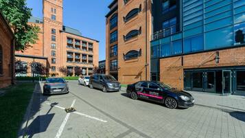 A parking area with multiple cars, a brick building with a tower, and a modern glass building.