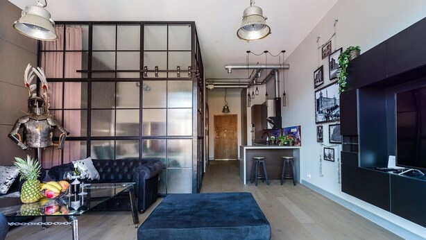 A modern living room with a black sofa, a glass coffee table with fruits, and a blue ottoman. - Loft Flat in Historical Area (Łódź)