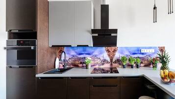 A modern kitchen with built-in appliances, a backsplash with a cityscape, and a fruit bowl on the counter.