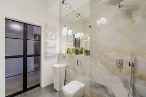 A modern bathroom with a glass shower enclosure, a white sink, and a mirror with decorative lights. - Loft Flat in Historical Area (Łódź)