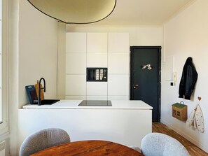 A compact kitchen with a central island, a black door, and a small basket decoration on the wall. - Lila Loft Bordeaux - Air-Conditioned Apartment in the Heart of the City Center (Bordeaux)