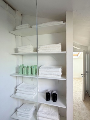 Een badkamer met witte planken waarop opgevouwen handdoeken en toiletartikelen liggen.